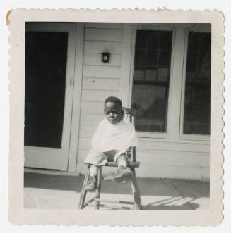 [Young boy seated on a chair outside]