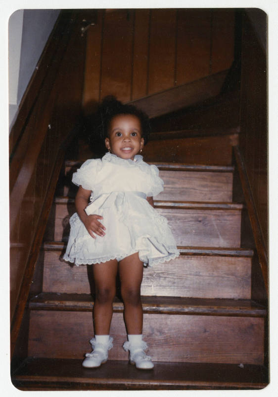 [Young girl standing on steps indoors]