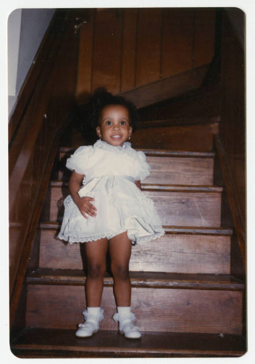 [Young girl standing on steps indoors]