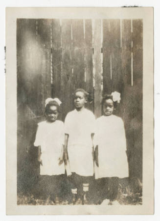 [Three young girls standing in front of a fence]