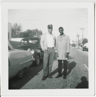 [Two men standing outside next to cars]