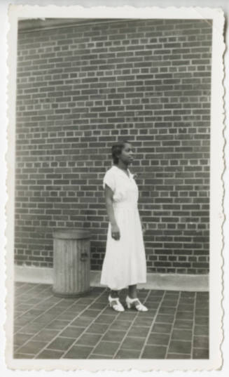 [Young woman standing against a wall]