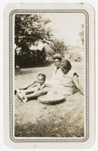 [Two women and a girl sitting on a lawn]