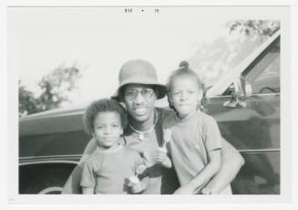 [Man and two children in front of a car]