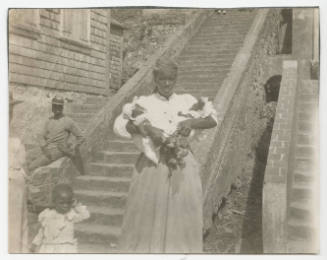 [Woman with two small babies, man, and young girl in front of stairs]
