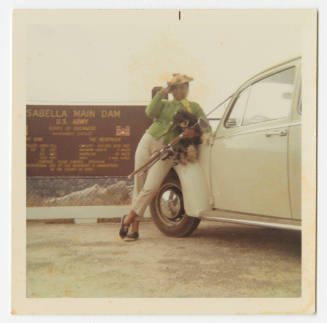 [Woman leaning against a car, holding dog and fishing pole, Lake Isabella, CA]