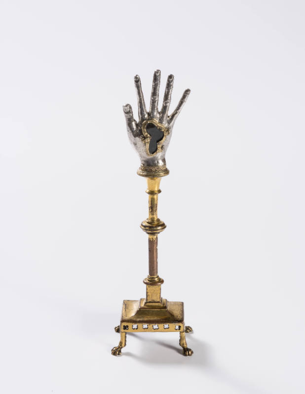 A repousséd silver hand reliquary raised on a gilded copper stand