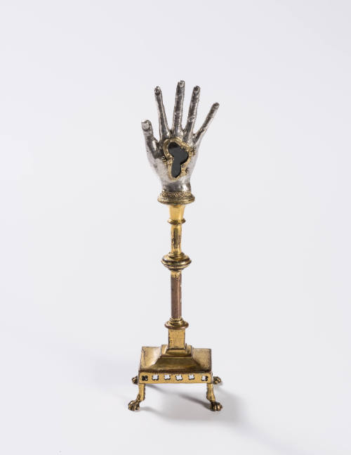 A repousséd silver hand reliquary raised on a gilded copper stand